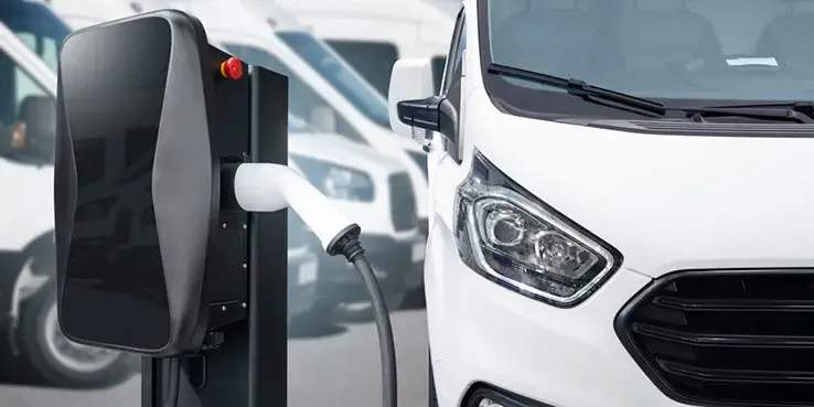 A white electric van is plugged into a charging point