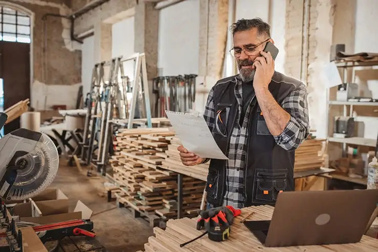 A tradesman on the phone holding an invoice in his workshop