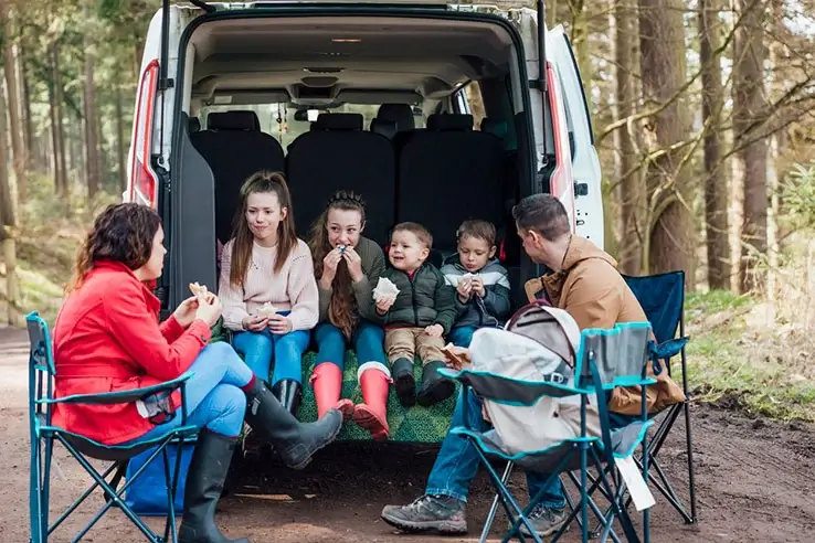 a family sitting together eating a packed lunch in the boot of a van
