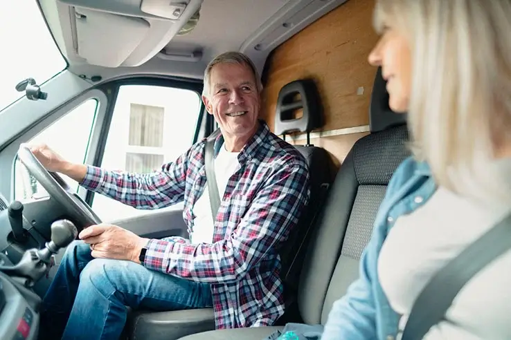 A man in the driver's seat of a van is smiling at a woman in the passenger seat.