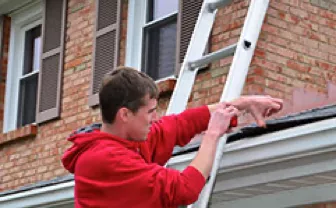 A man cleaning a roof, standing on a ladder