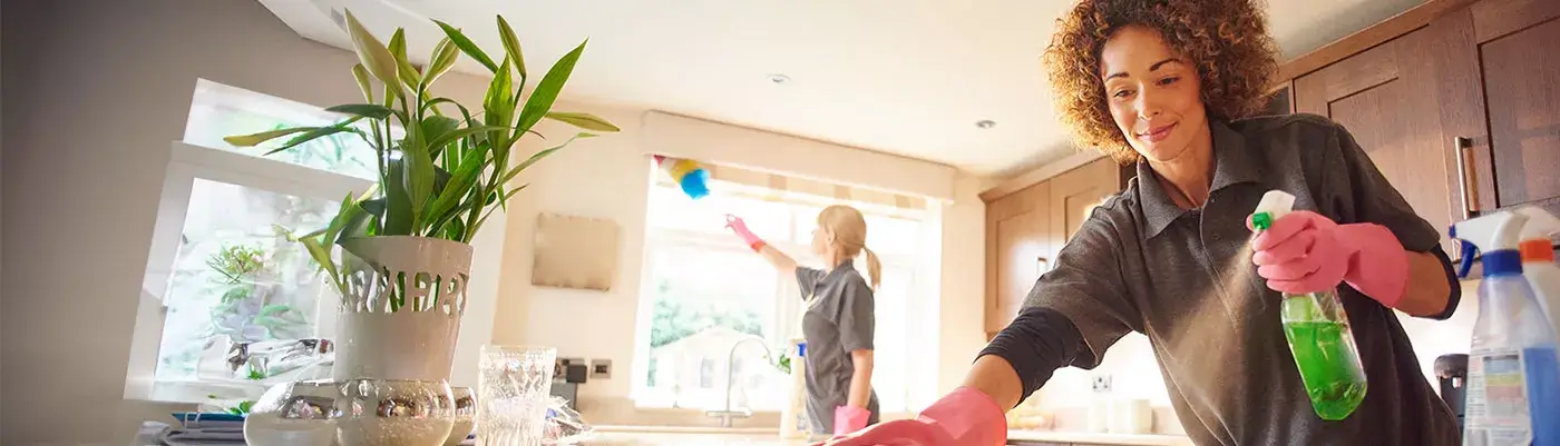 a professional cleaner in a kitchen spraying a cleaning product onto a worktop