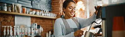 smiling female barista making coffee behind a counter in a coffee shop