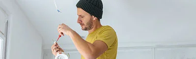 an electrician is fixing and changing ceiling lights standing on a ladder