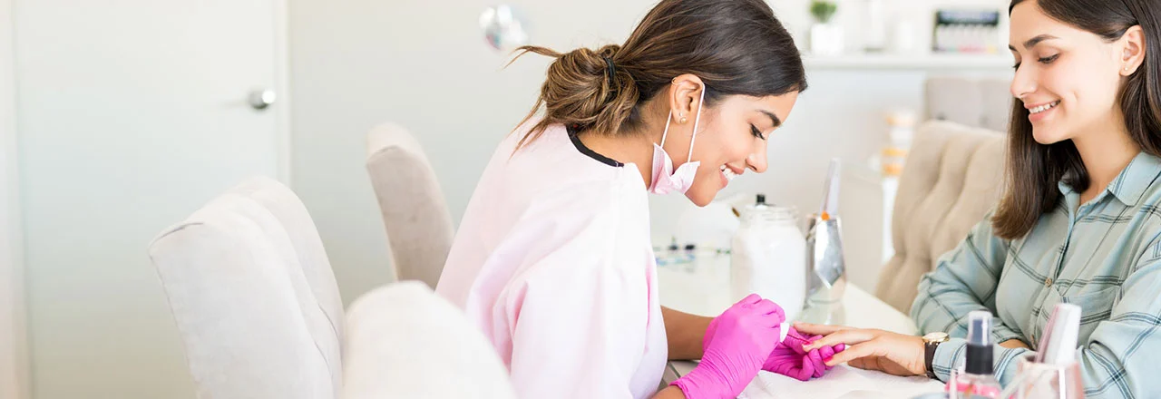 A beautician is painting a woman's nails in a salon.