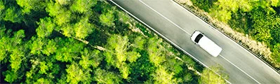 A bird's-eye view of a white van driving down a tree-lined road.